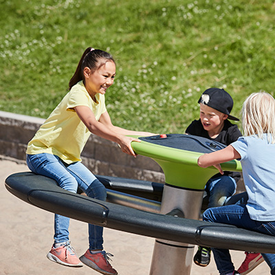 Des enfants tournent sur le rond-point d'une aire de jeux.